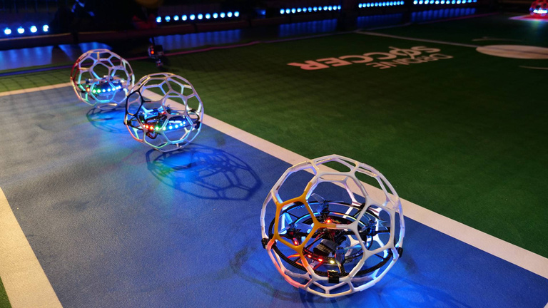 Match de drones soccer avec cages sphériques dans un terrain grillagé